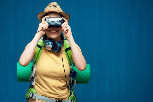 woman traveler with backpack holding photo camera on blue background  - Foto, afbeelding