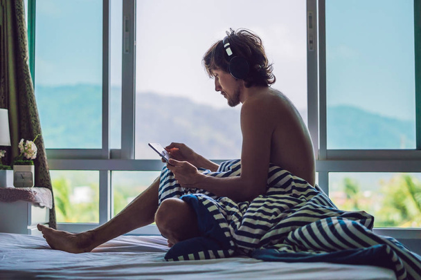 Man woke up in the morning and reads the news on the tablet in the background of a window with a view to the mountains. - Zdjęcie, obraz