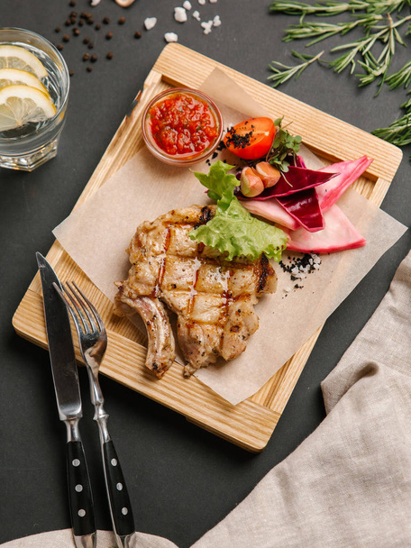 Gegrild varkensvlees met bloemkool, sla, tomaat, knoflook en barbecue saus geserveerd op houten schotel met perkamentpapier, limonade, mes en vork - Foto, afbeelding