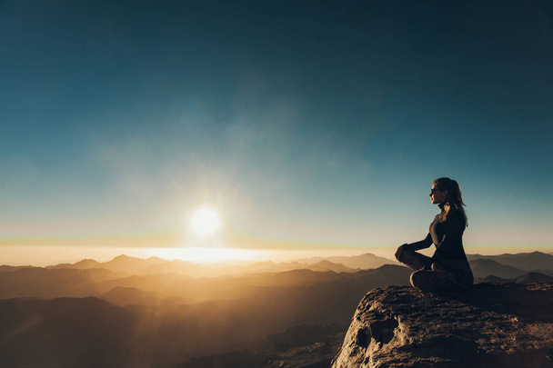 Femme assise dans une pose de yoga sur le mont Sinaï et médite sur fond de lever de soleil
. - Photo, image