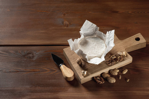 close-up of delicious white Camembert cheese on wooden cutting board with nuts and knife - Φωτογραφία, εικόνα