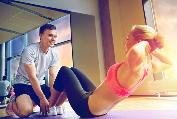 woman with personal trainer doing sit ups in gym - Fotoğraf, Görsel