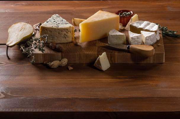 close-up of delicious cheese set of Parmesan, Camembert and Blue cheese with nuts, spices and knife on wooden cutting board on table background - Photo, image