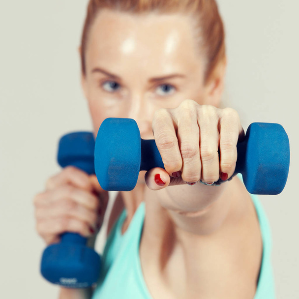 middle-aged woman working out with dumbbells in front of her face - Φωτογραφία, εικόνα