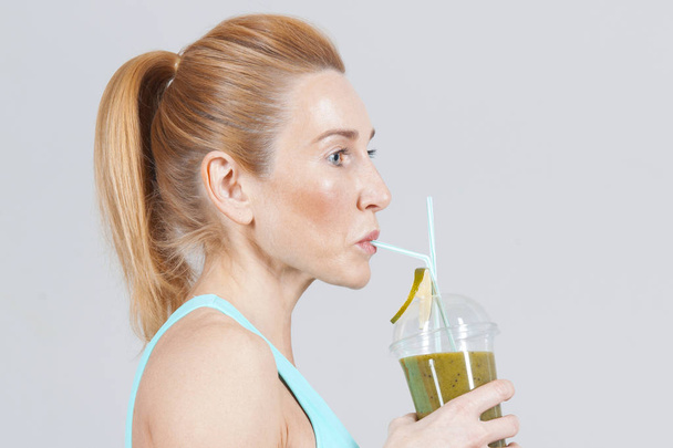middle-aged sports woman drinking the fruit smoothie on the grey background  - Valokuva, kuva