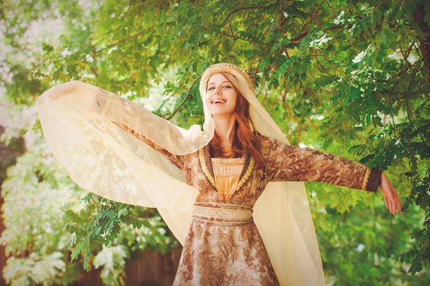 Молода щаслива середньовічна дівчина біля зелених гілок дерева
.  - Фото, зображення