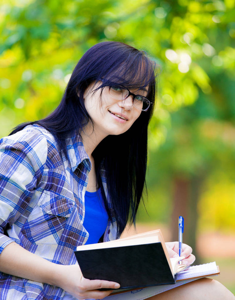 Jovem menina estudante morena com cadernos estudando na grama verde no verão
 - Foto, Imagem