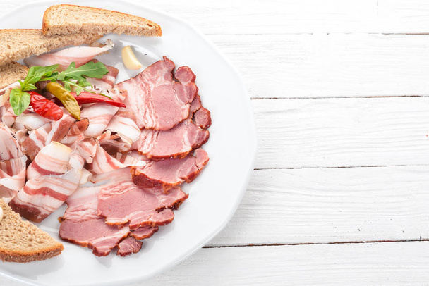 Slice of smoked meat on a plate. On a wooden background. Top view. Copy space. - Photo, image