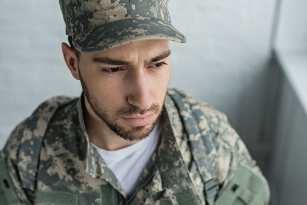 Portret van soldaat in militaire uniform op zoek weg tegen witte bakstenen muur - Foto, afbeelding