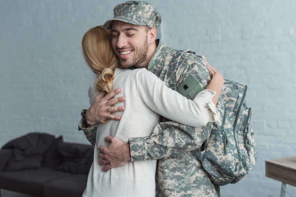 side view of smiling man in military uniform and mother hugging each other at home - Fotoğraf, Görsel