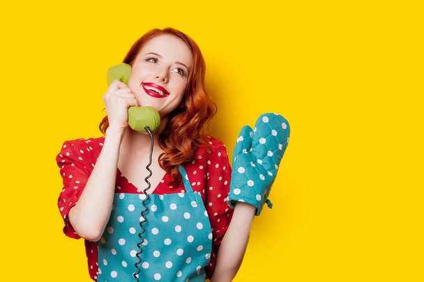 Redhead νοικοκυρά με το ακουστικό του τηλεφώνου κλήσης σε κίτρινο φόντο - Φωτογραφία, εικόνα