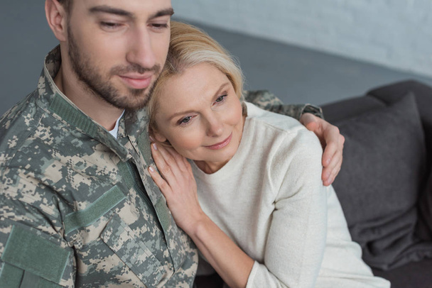 portrait of man in military uniform hugging smiling mother at home - Foto, afbeelding
