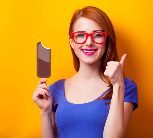 Portrait of a young redhead girl with chocolate ice-cream on yellow background  - Foto, Imagen