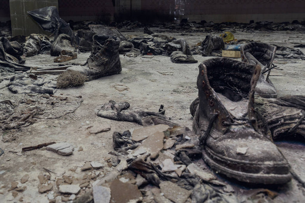 alte Schuhe auf staubigem Boden in einem kriegszerstörten Haus, ruiniertes dunkles Gebäude im Inneren, Nachwirkungen von Katastrophen - Foto, Bild