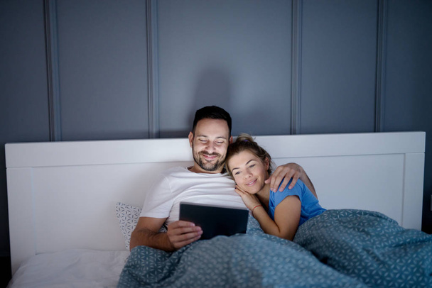 happy young love couple lying in bed and watching movie via tablet pc together - Foto, imagen