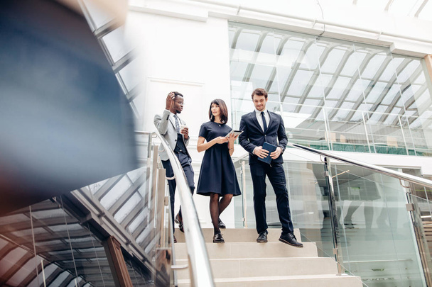 Three multiracial business people walking down on stairs with digital tablet - 写真・画像