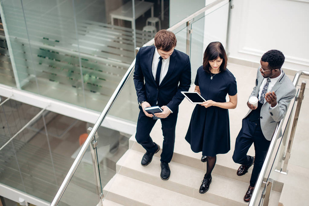 Three multiracial business people walking down on stairs with digital tablet - Photo, image