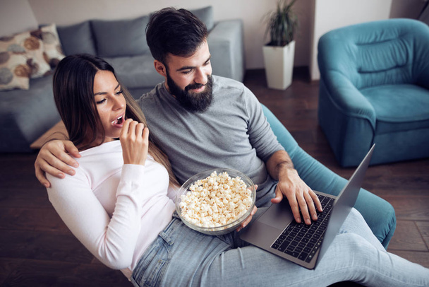 Giovane coppia seduta in soggiorno e utilizzando il computer portatile, guardando il film
. - Foto, immagini
