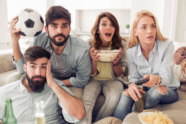 Vrolijke groep vrienden voetbalwedstrijd op tv kijken, plezier thuis. - Foto, afbeelding