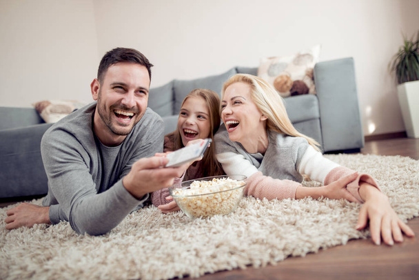 Padre, Mather y su hija tumbados en el suelo, viendo la televisión y comiendo palomitas de maíz
. - Foto, imagen