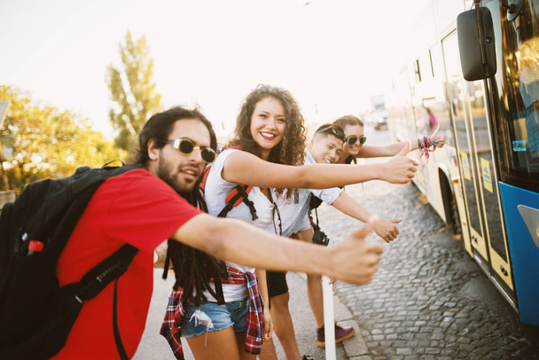 Grupa młodych przyjaciół happy podróżujących razem i autostopem, próbując złapać autobus - Zdjęcie, obraz