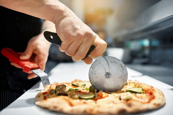 cook cutting pizza to pieces at pizzeria - Zdjęcie, obraz