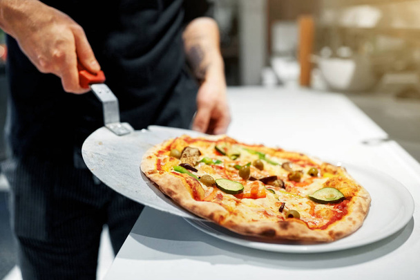 cook with baked pizza on peel at pizzeria - Foto, afbeelding