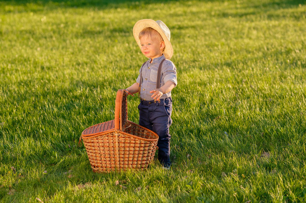 Portrait of toddler child outdoors. Rural scene with one year old baby boy wearing straw hat and picnic basket - Photo, Image
