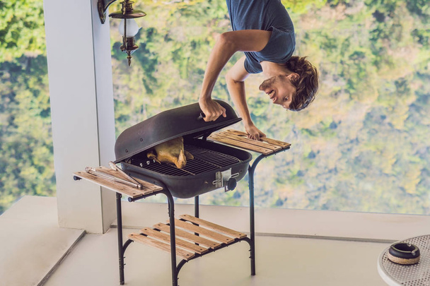 Handsome man preparing barbecue for friends standing upside down. - Foto, afbeelding