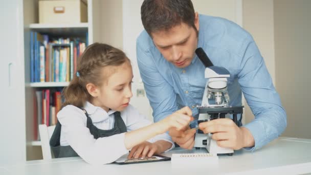 Маленька дівчинка з учителем на уроці науки з мікроскопом на столі
. - Кадри, відео