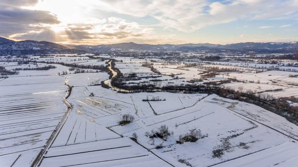 Aerial view of river flowing through snow covered countryside at sunset. - Фото, изображение