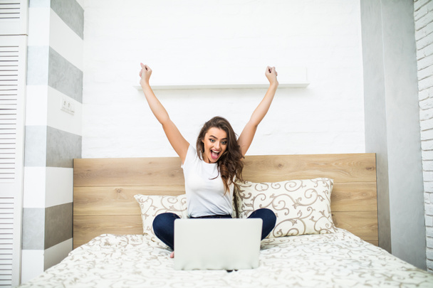 Chica con las manos levantadas en la cama usando el ordenador portátil en casa
 - Foto, imagen