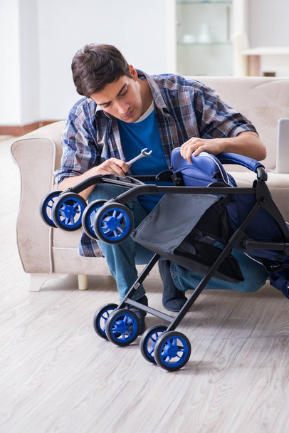Młody ojciec montujący dziecięcy wózek w domu - Zdjęcie, obraz
