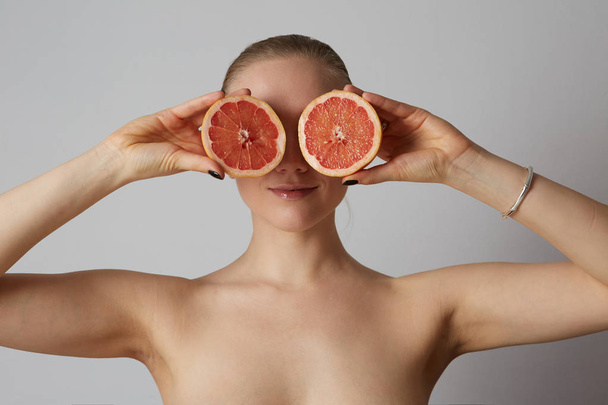 Close up portrait the blonde woman holding half an orange isolated on the white background - Zdjęcie, obraz