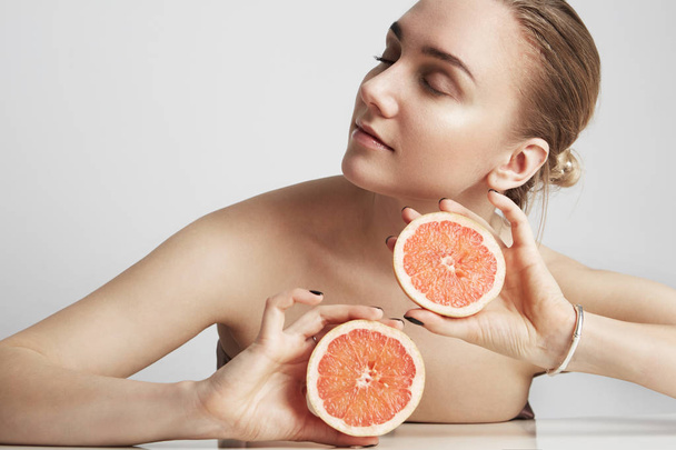 Close up portrait the blonde woman holding half an orange isolated on the white background. Beauty concept - Foto, immagini