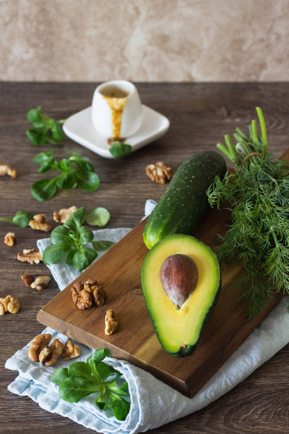 Ingredients for green salad (avocado, cucumbers, corn salad, apple, walnuts and dill) with olive oil mustard sauce on wooden background. Diet or healthy food concept. Space for text. - Foto, Imagen