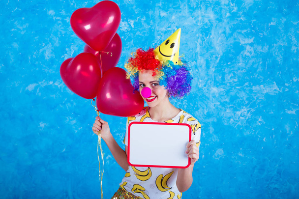 Happy clown. Concept of holidays. A cheerful young girl in a clown suit posing in front of a camera on a blue background. 1 April Fools' Day concept. Birthday. - Фото, зображення