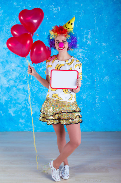 Happy clown. Concept of holidays. A cheerful young girl in a clown suit posing in front of a camera on a blue background. 1 April Fools' Day concept. Birthday. - Фото, изображение