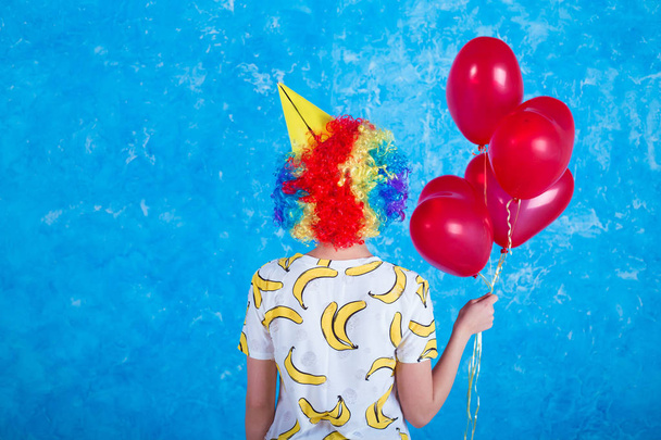 Happy clown. Concept of holidays. A cheerful young girl in a clown suit posing in front of a camera on a blue background. 1 April Fools' Day concept. Birthday. - Foto, immagini