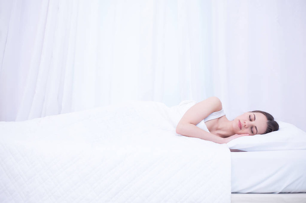 Young beautiful smiling woman is sleeping sweetly in a white bed at home. Relax and rest. - Foto, afbeelding