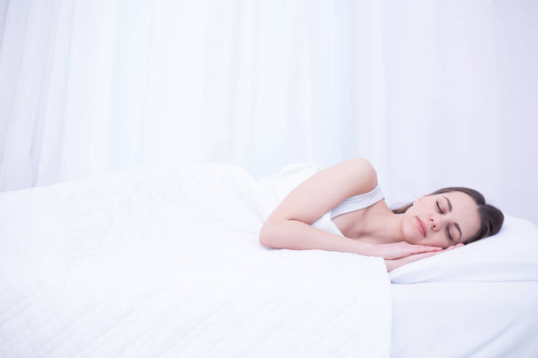 Young beautiful smiling woman is sleeping sweetly in a white bed at home. Relax and rest. - Foto, imagen