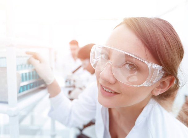 Young woman scientist in protective glasses holding test tubes - Foto, Imagen
