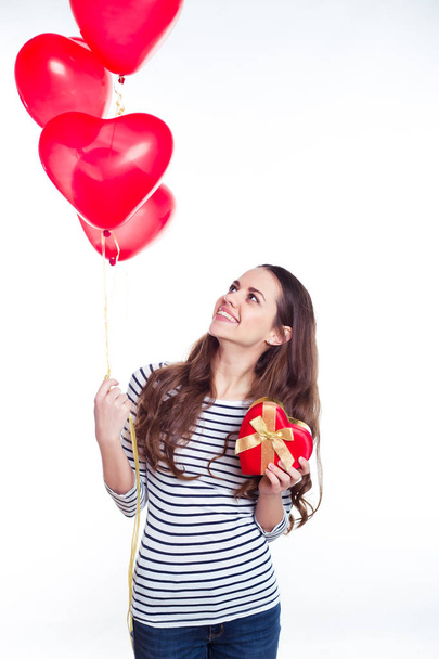 Dárky pro milované. Krásná usměvavá mladá žena v neformálním oblečení s helium balónky a dárek v podobě srdce ve svých rukou. Den svatého Valentýna. Narozeniny. - Fotografie, Obrázek