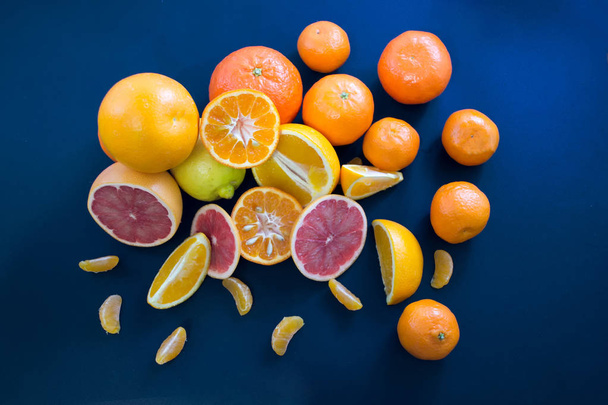 Colored Citrus fruits on a dark blue background. Slices of citrus and peel. Citrus reticulata. Citrus paradisi. Citrus limon. Citrus sinensis.  - Photo, Image