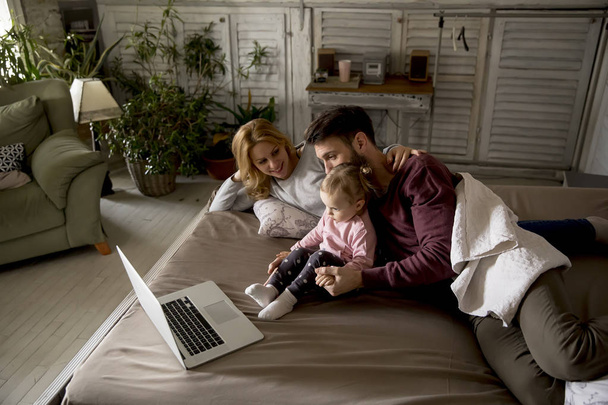 Família feliz jaz na cama e assistindo algo no laptop no quarto
 - Foto, Imagem
