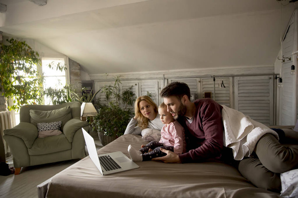 Happy family lies on bed and watching something on laptop in the bedroom - Photo, Image