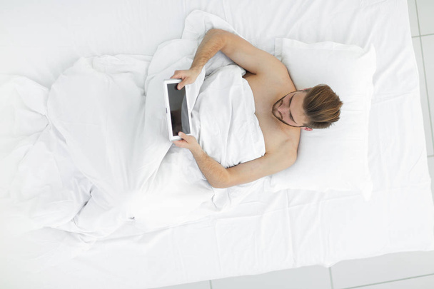 smiling man using digital tablet lying on bed - Photo, image