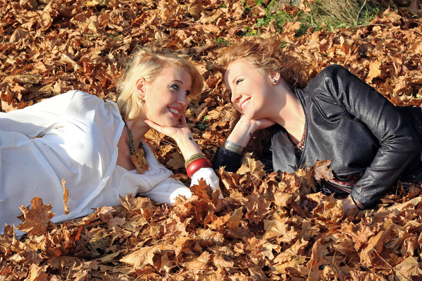 Pretty young sisters lie together in autumn in the foliage - Photo, Image