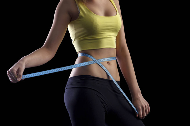 Happy fitness girl measuring her waistline over black background - Photo, Image