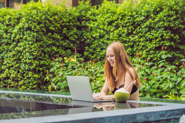 Young female freelancer sitting near the pool with her laptop in the hotel browsing in her smartphone. Busy at holidays. Distant work concept. Copy space for your text. - Foto, Imagem